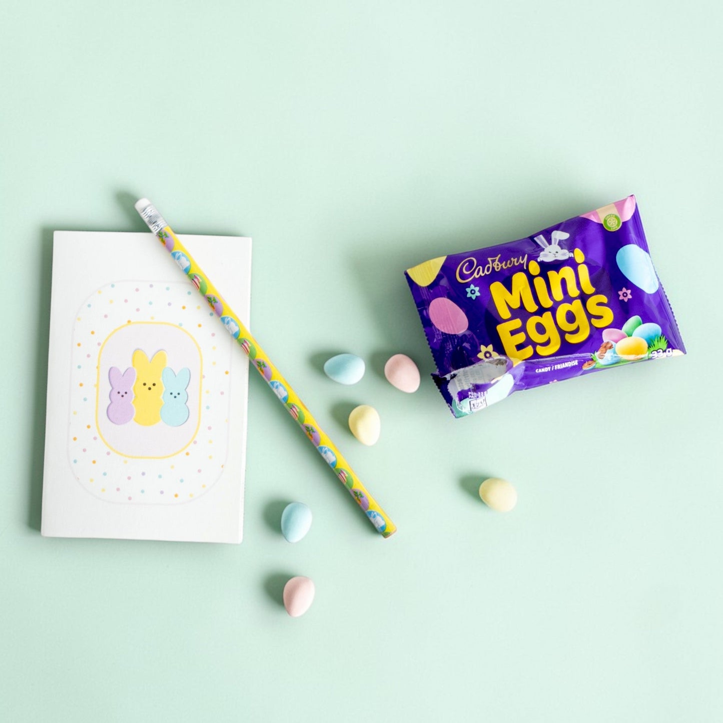 Cadbury Mini Eggs packaging with a pencil and notebook on a light green background